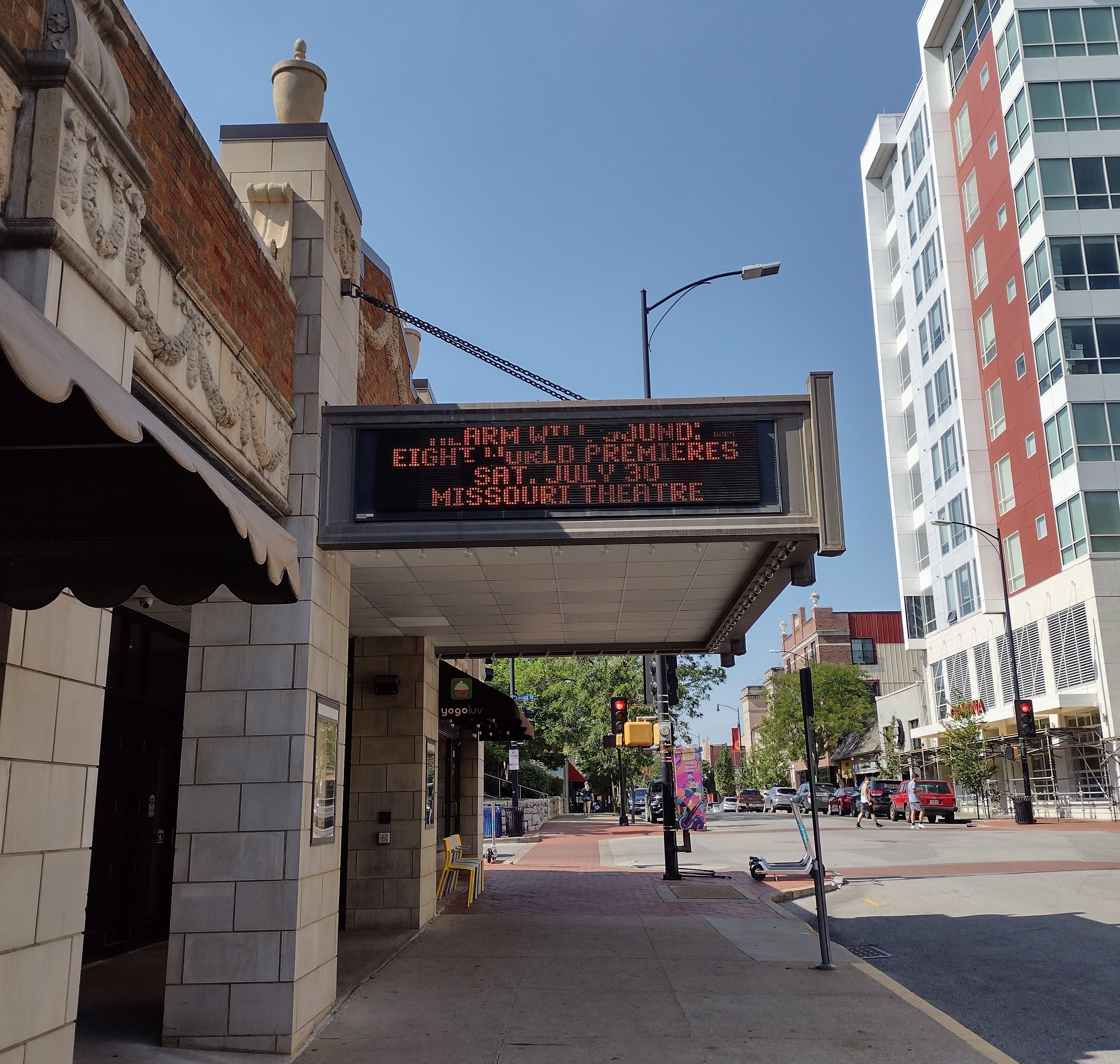 The marquee of the Missouri Theater reads "ALARM WILL SOUND; EIGHT WORLD PREMIERES; SAT, JULY 30; MISSOURI THEATER" with a clear blue sky behind it. Some pixels are missing so the text is hard to read.
